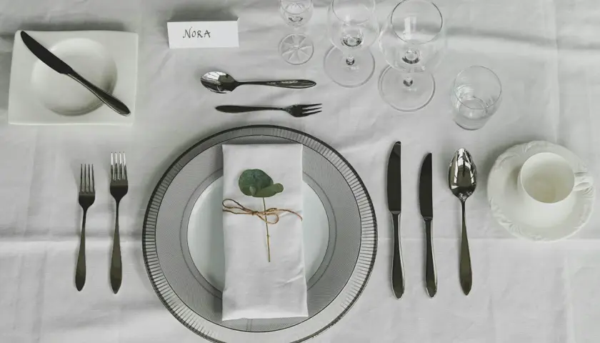 Elegante Tischdeko: besteck auflegen nur messer und gabel, mit Namenskarte "Nora" und einem grünen Blatt auf der Serviette.