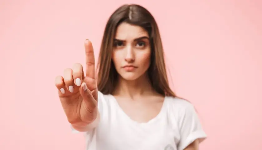 Frau hebt den Zeigefinger, als ob sie eine Einladung ablehnt. Ihre Miene ist ernst, die Antwort auf Absage Einladung ist klar.