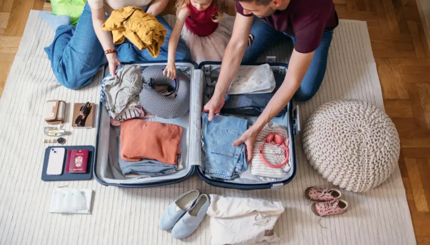 Familie packt gemeinsam eine Reisetasche. Kleidung, Nackenkissen und Reiseutensilien werden sorgfältig verstaut.