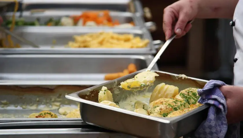 Eine Hand schöpft Kartoffeln aus einer Chafing Dish. Da fragt man sich, warum sagt man Mahlzeit? Leckeres Essen für alle!