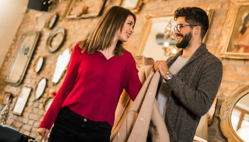 Ein Gentleman und eine Frau schauen sich lächelnd an, während sie Kleidung in einem Geschäft betrachten.
