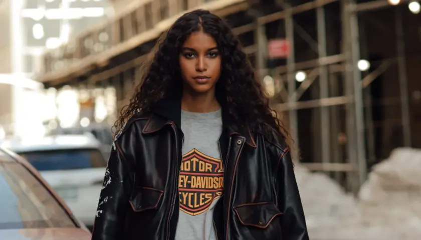 Junge Frau mit langen, lockigen Haaren trägt eine Lederjacke über einem Harley-Davidson-Shirt im Millennials-Style.