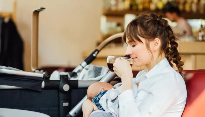 Eine junge Mutter genießt eine Tasse Kaffee, während sie ihr Baby stillt. Der Kinderwagen steht daneben. Ein Moment der Ruhe beim Stillen im Restaurant.