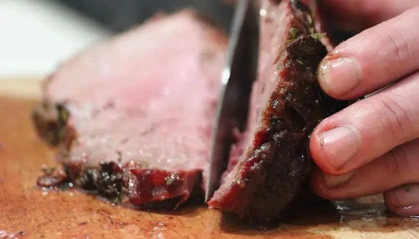 Ein Messer schneidet ein saftiges Steak auf einem Holzbrett. So schneidet man ein Steak richtig, um die zarten Fasern zu erhalten.