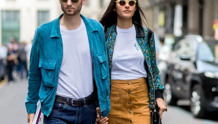 Ein Paar geht Hand in Hand, bereit für ein erstes Date. Er trägt eine blaue Jacke, sie einen gemusterten Blazer.