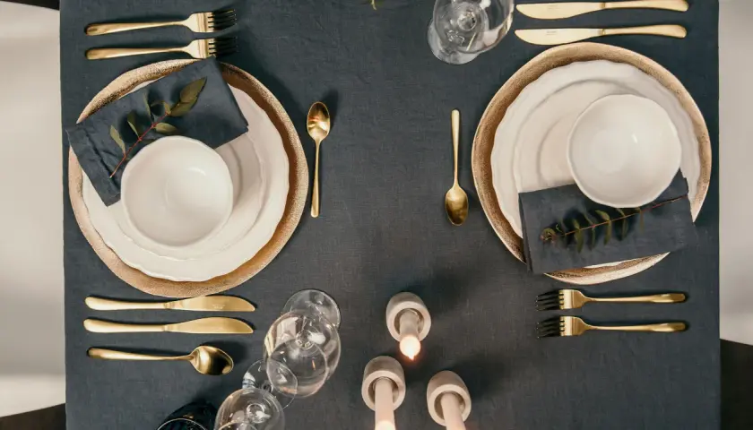 Elegante Tischdeko mit goldenem Besteck, das den Knigge-Regeln folgt. Teller, Gläser und Kerzen sorgen für festliche Stimmung.