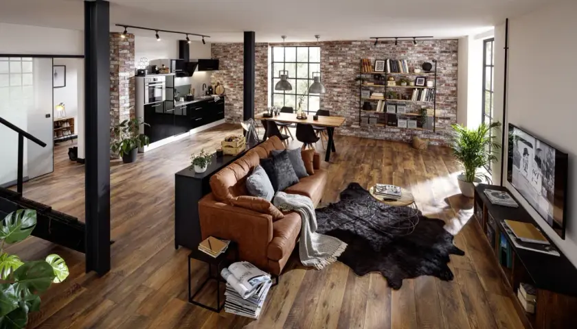 Gemütliche, offene industrial wohnung mit brauner Ledercouch, Holztisch, schwarzer Küche und Ziegelwänden.