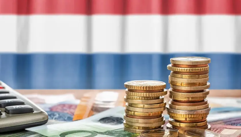 Münzen und Geldscheine liegen auf einem Tisch, im Hintergrund die niederländische Flagge. Ein Taschenrechner deutet auf die Berechnung von Trinkgeld in Holland.