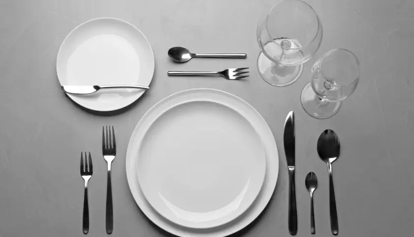 Einfach den Tisch decken: Zwei weiße Teller, Besteck und Weingläser liegen bereit für ein schönes Essen.