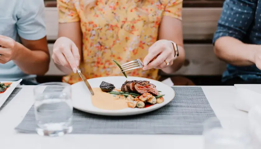 Gutes Benehmen bei Tisch: Eine Frau isst ein Steak mit Beilagen, während sie sich mit ihren Begleitern unterhält.