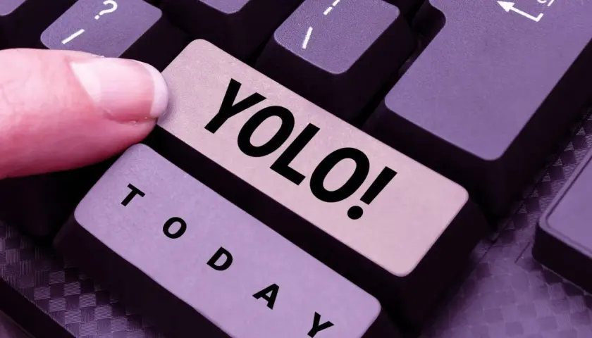 Ein Finger drückt die Taste "YOLO!". Was heißt YOLO? Das Leben ist kurz, also nutze den Tag!