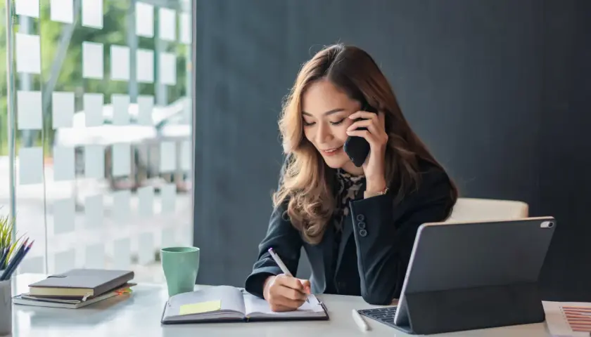 Eine Geschäftsfrau telefoniert und macht sich Notizen. Sie zeigt, wie man richtig telefonieren kann, während sie konzentriert arbeitet.