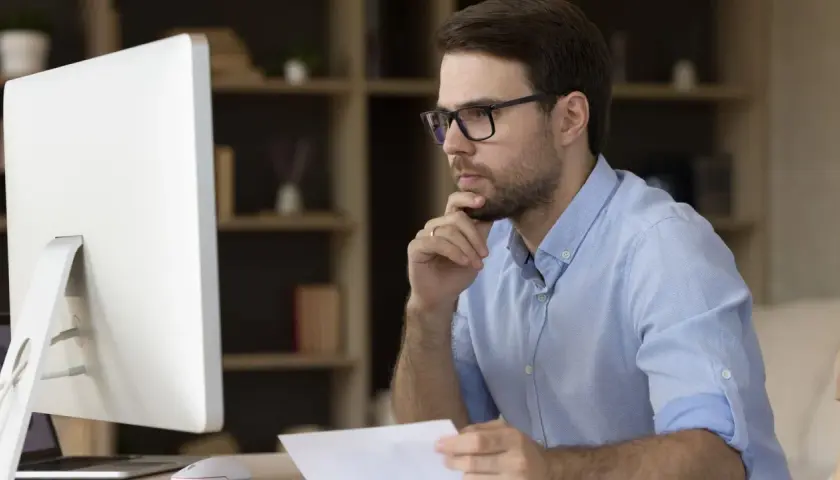 Mann mit Brille am Schreibtisch, der nachdenklich auf den Bildschirm blickt, um alle Mails in Outlook anzuzeigen.