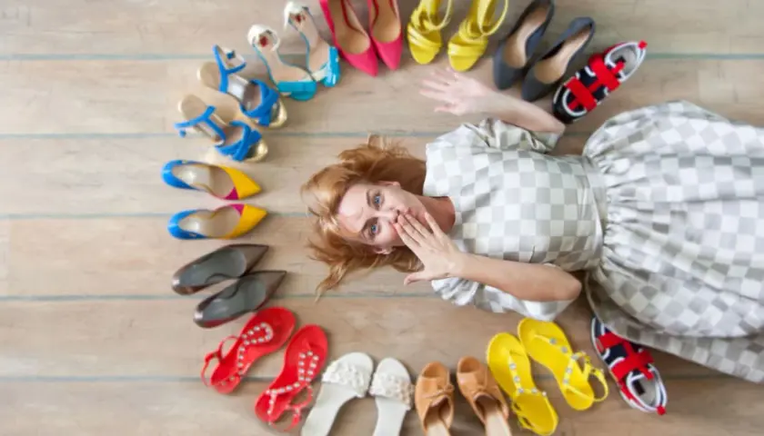 Frau liegt inmitten einer bunten Schuhsammlung, die sie gerade aussortiert. Von High Heels bis Sneakern ist alles dabei.