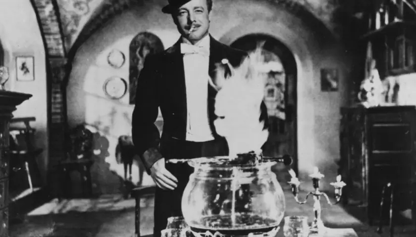 Mann in Zylinder und Smoking bereitet Feuerzangenbowle zu. Flammen lodern über dem Kessel. So trinkt man Feuerzangenbowle!