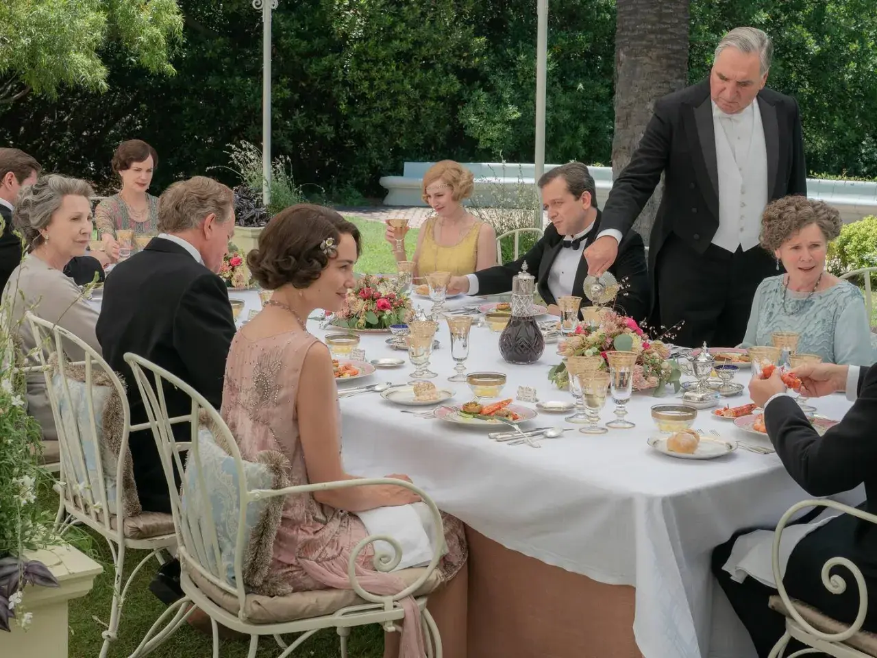 Gäste speisen im Freien, ein Butler serviert. Alle zeigen gute Manieren bei diesem eleganten Festessen.