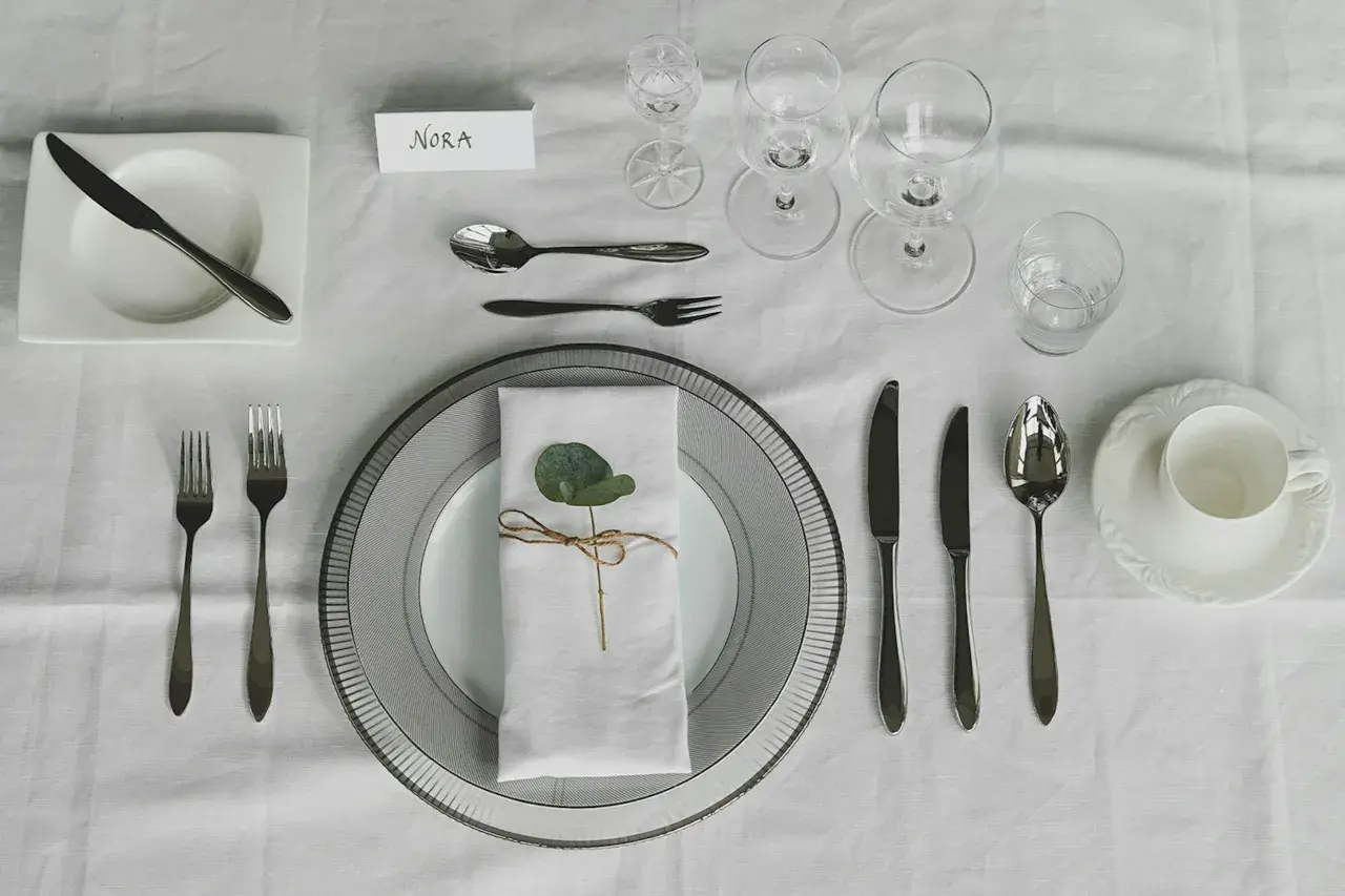 Elegante Tischdeko: besteck auflegen nur messer und gabel, mit Namenskarte "Nora" und einem grünen Blatt auf der Serviette.