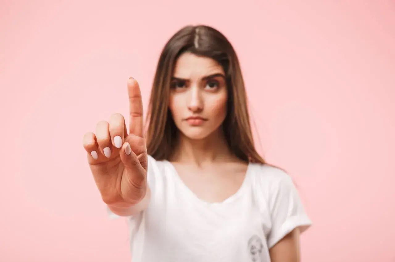 Frau hebt den Zeigefinger, als ob sie eine Einladung ablehnt. Ihre Miene ist ernst, die Antwort auf Absage Einladung ist klar.