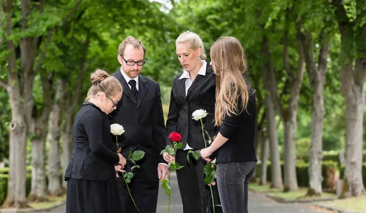 Trauernde Familie mit Rosen bei einer Beerdigung. Der Knigge zur Beerdigung wird hier durch stille Anteilnahme und respektvolles Gedenken gezeigt.