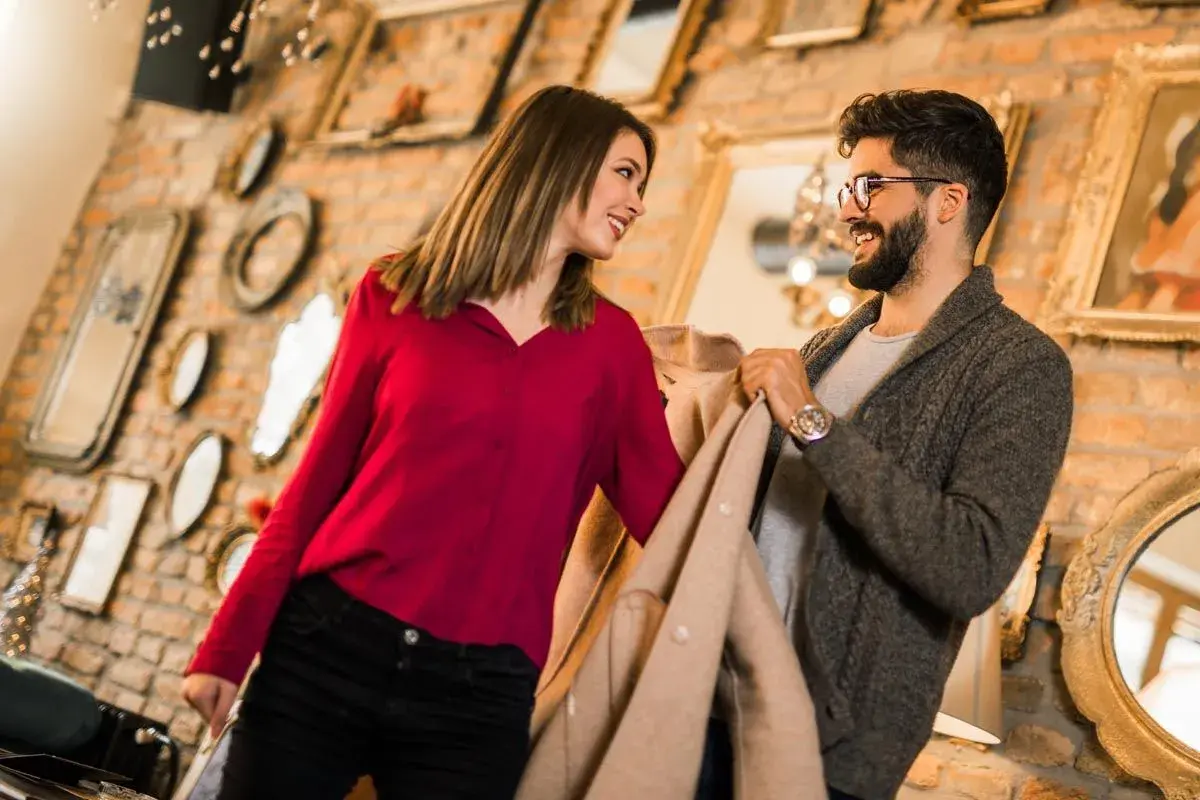 Ein Gentleman und eine Frau schauen sich lächelnd an, während sie Kleidung in einem Geschäft betrachten.