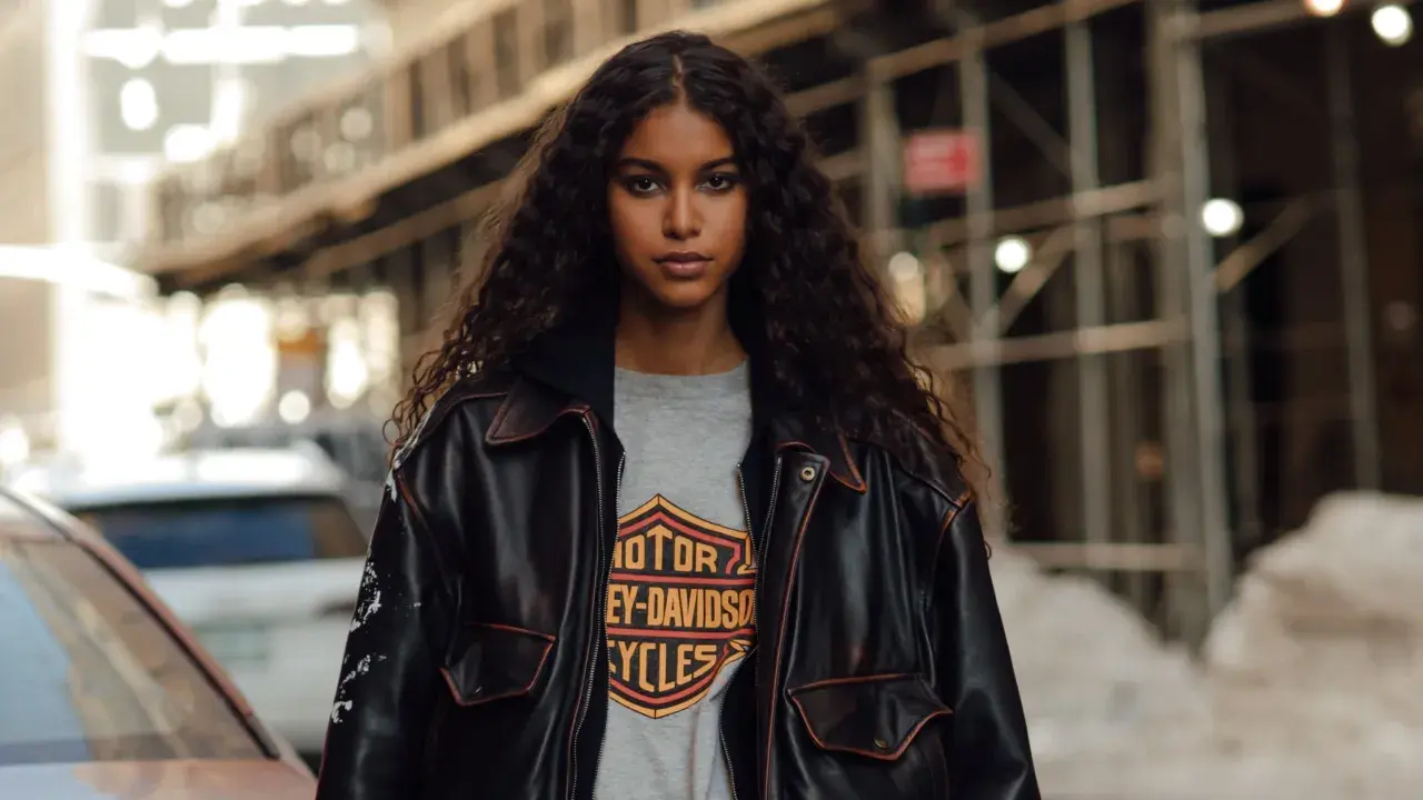 Junge Frau mit langen, lockigen Haaren trägt eine Lederjacke über einem Harley-Davidson-Shirt im Millennials-Style.