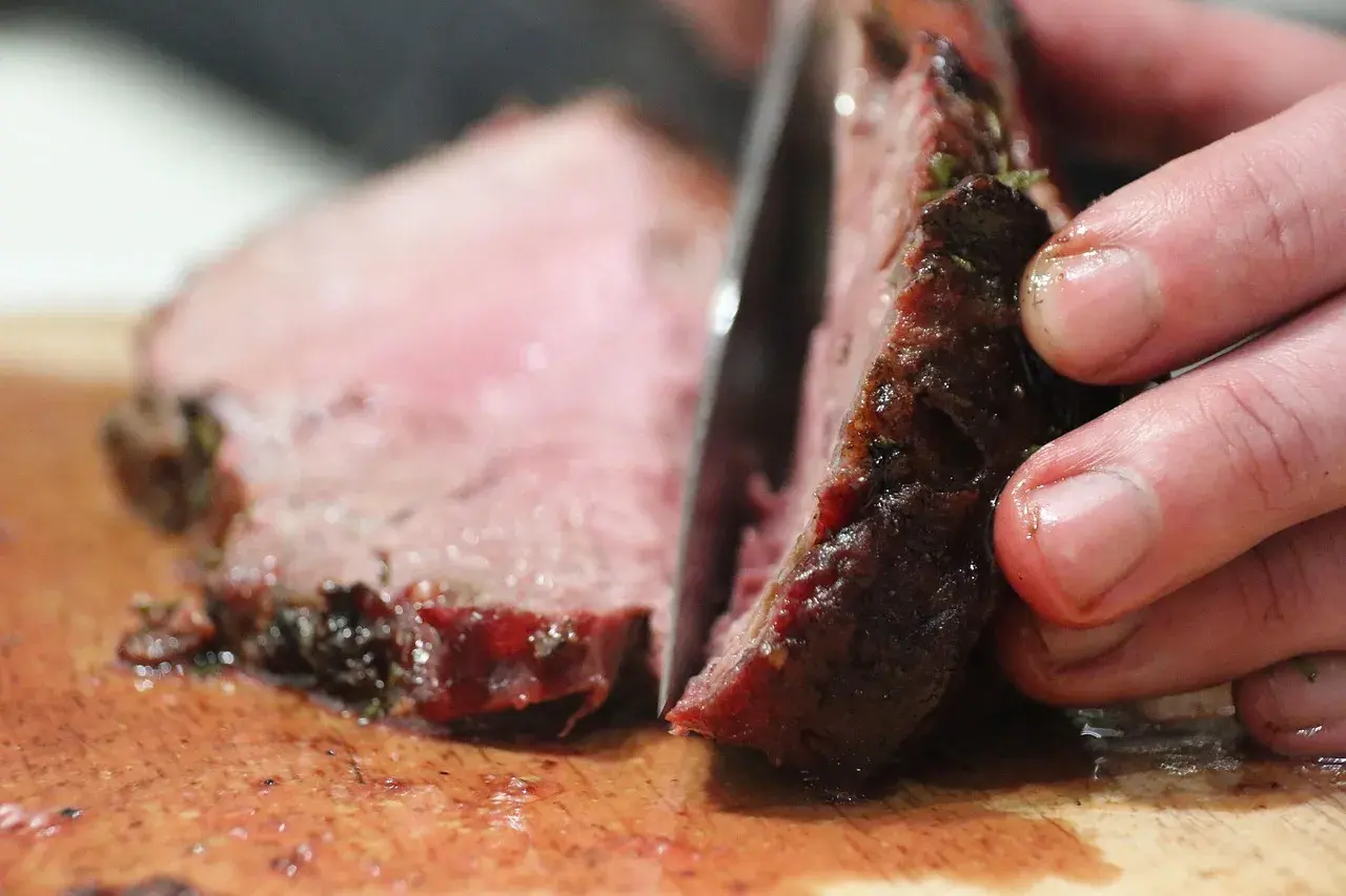 Ein Messer schneidet ein saftiges Steak auf einem Holzbrett. So schneidet man ein Steak richtig, um die zarten Fasern zu erhalten.