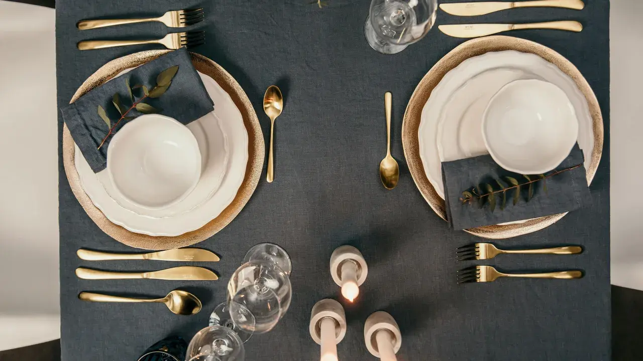 Elegante Tischdeko mit goldenem Besteck, das den Knigge-Regeln folgt. Teller, Gläser und Kerzen sorgen für festliche Stimmung.