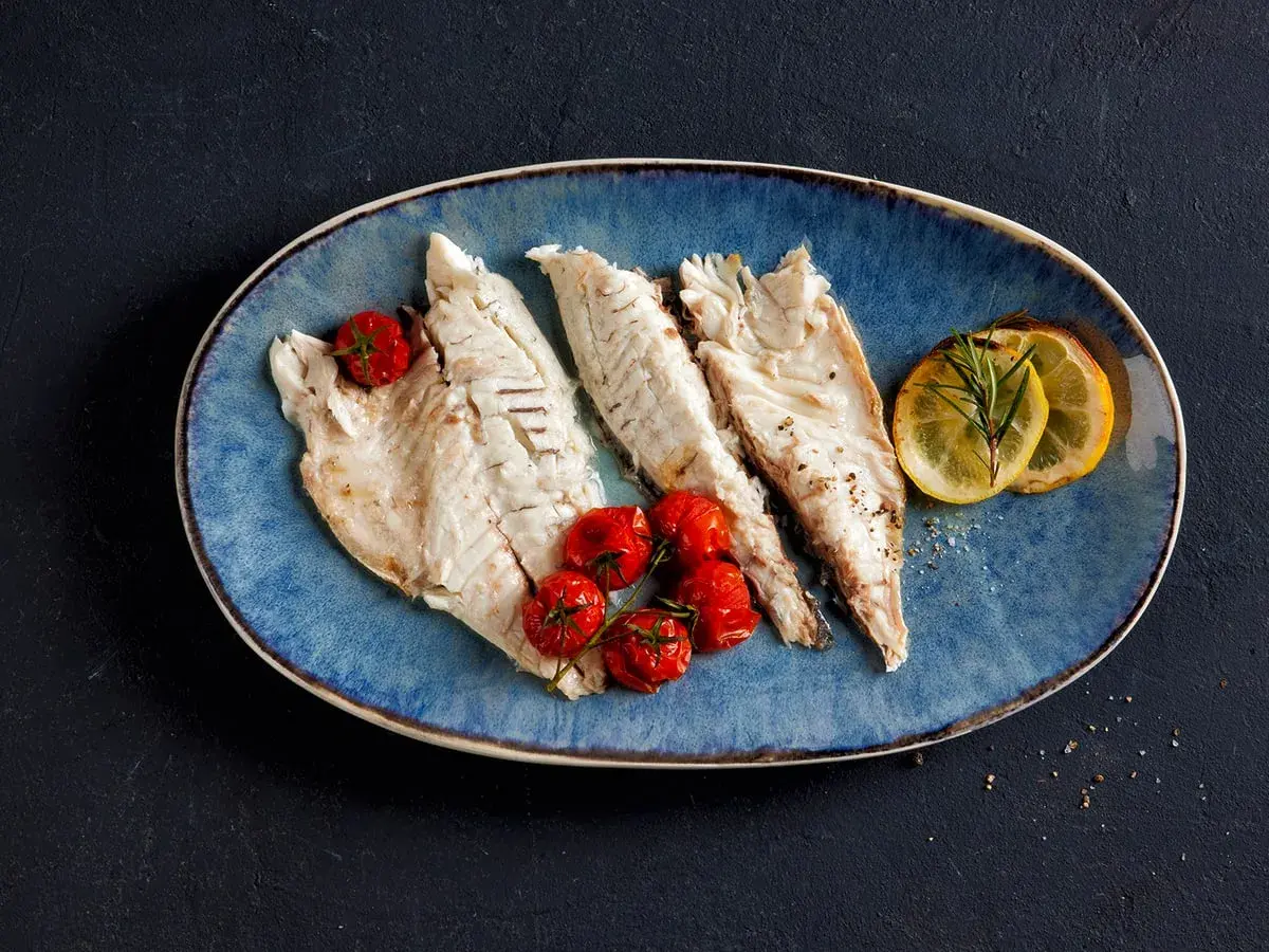 Drei zarte Fischfilets liegen auf einem blauen Teller, garniert mit Kirschtomaten und Zitronenscheiben. Perfekt zum Fisch filetieren am Tisch.
