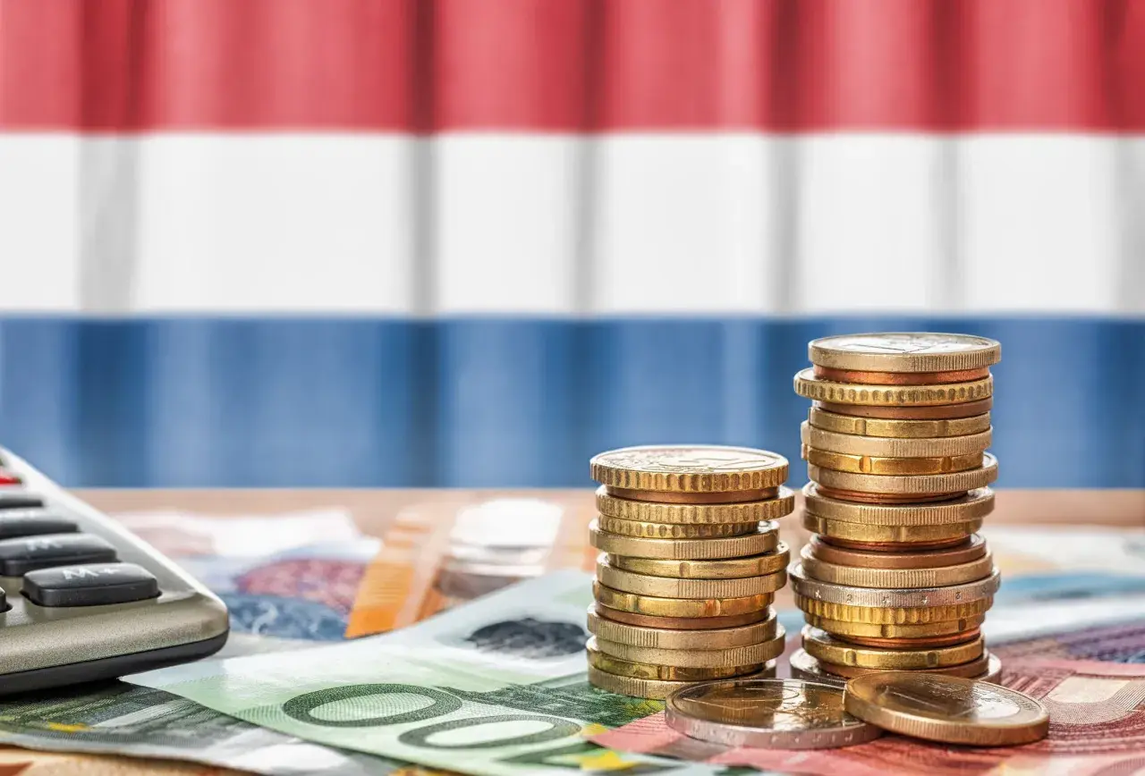 Münzen und Geldscheine liegen auf einem Tisch, im Hintergrund die niederländische Flagge. Ein Taschenrechner deutet auf die Berechnung von Trinkgeld in Holland.