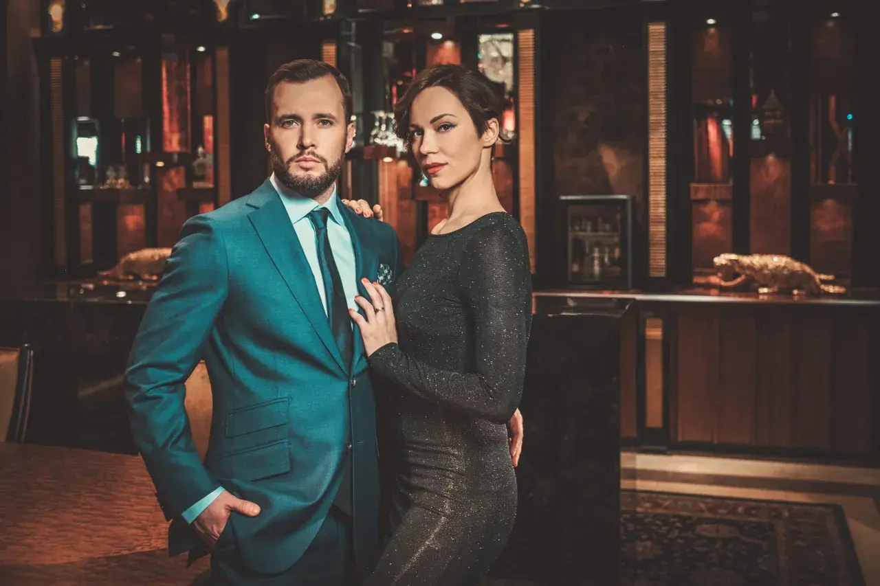 Ein eleganter englischer Gentleman im Anzug posiert mit einer Frau in einem glitzernden Kleid in einem luxuriösen Interieur.