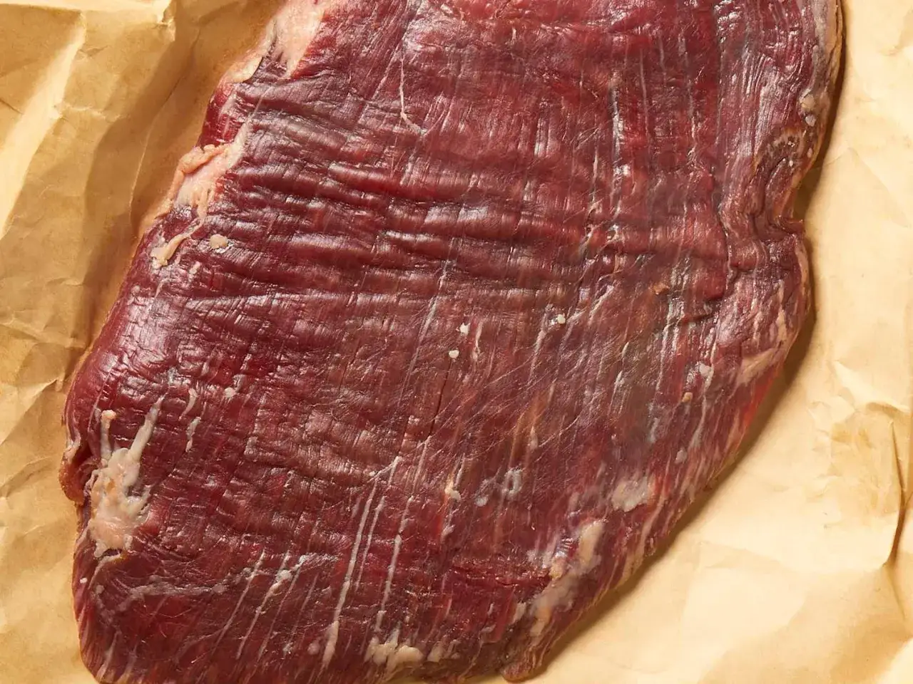 Rohes Flanksteak auf Backpapier. F&uuml;r zartes Fleisch ist es wichtig, das steak richtig schneiden.