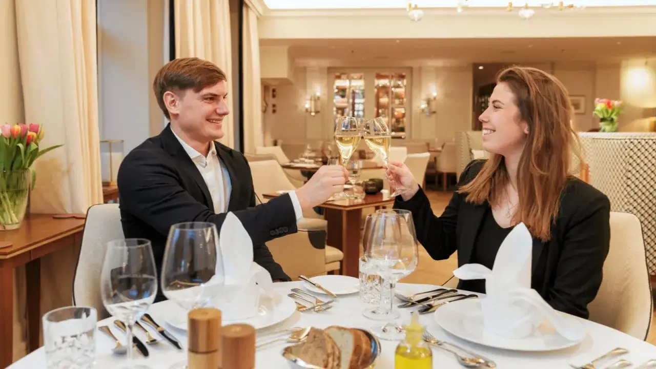 Ein Mann und eine Frau sto&szlig;en mit Champagner an. Die Frau sitzt rechts.