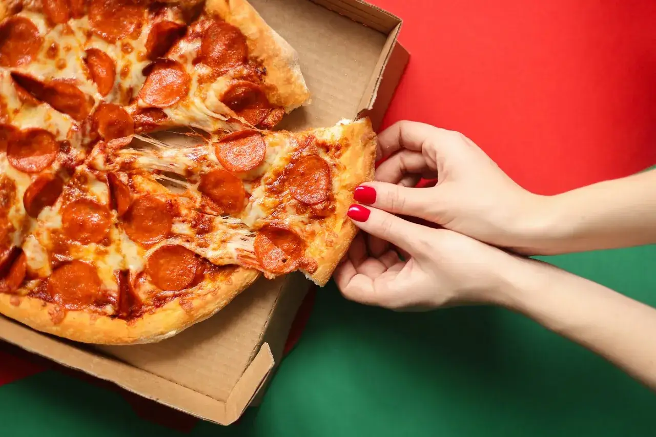 H&auml;nde greifen nach einem St&uuml;ck Pepperonipizza aus einer Pappschachtel. So isst man Pizza richtig &ndash; mit viel K&auml;se und leckeren Salamischeiben.