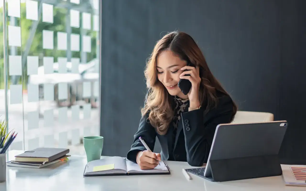 Frau im B&uuml;ro telefoniert und macht Notizen. Es ist Zeit zum Telefonieren, um wichtige Informationen festzuhalten.