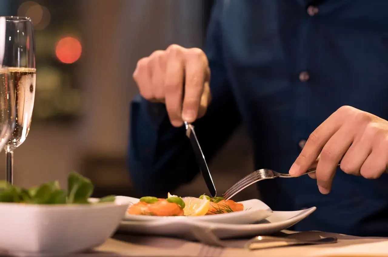 Mann isst Lachs mit Zitrone und Dill. Er sitzt am Tisch, neben ihm ein Glas Sekt und ein Salat.