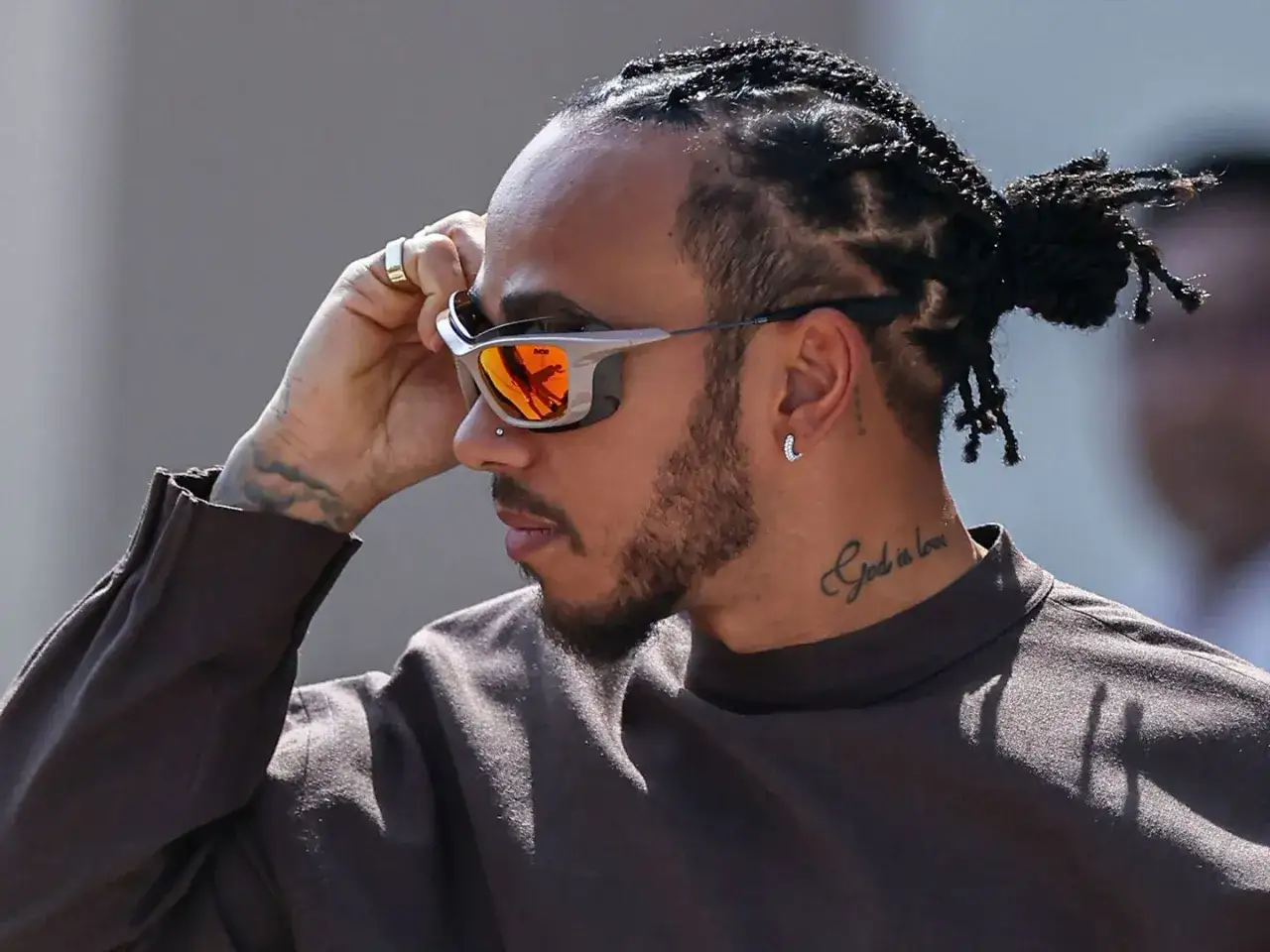 Mann mit geflochtenen Haaren und Bart, der eine trendige Sonnenbrille f&uuml;r Herren mit orangefarbenen Gl&auml;sern zurechtr&uuml;ckt.