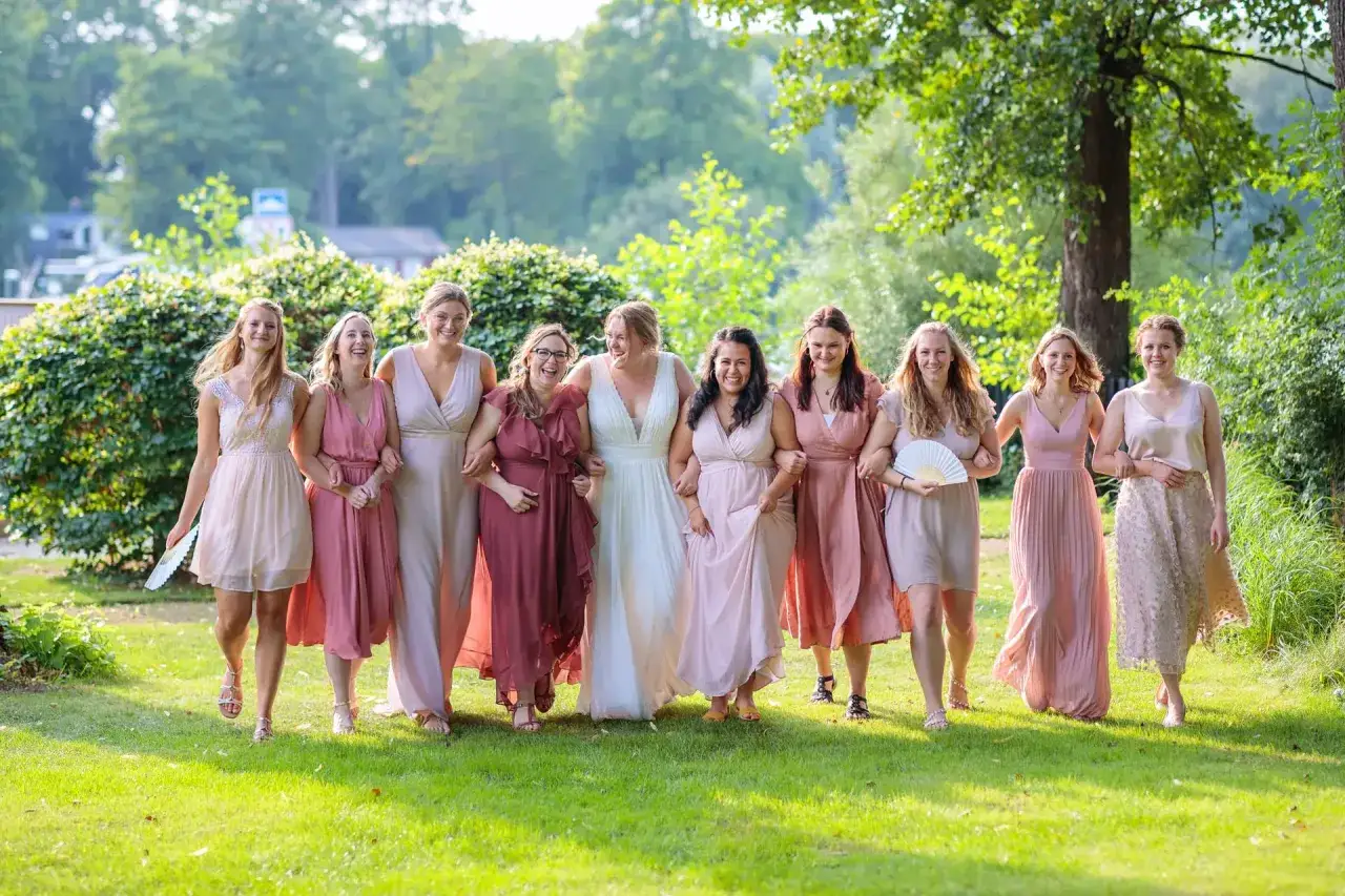 Brautjungfern in rosa Kleidern gehen Arm in Arm &uuml;ber eine gr&uuml;ne Wiese. Ein sch&ouml;nes Bild f&uuml;r den Hochzeitsknigge.
