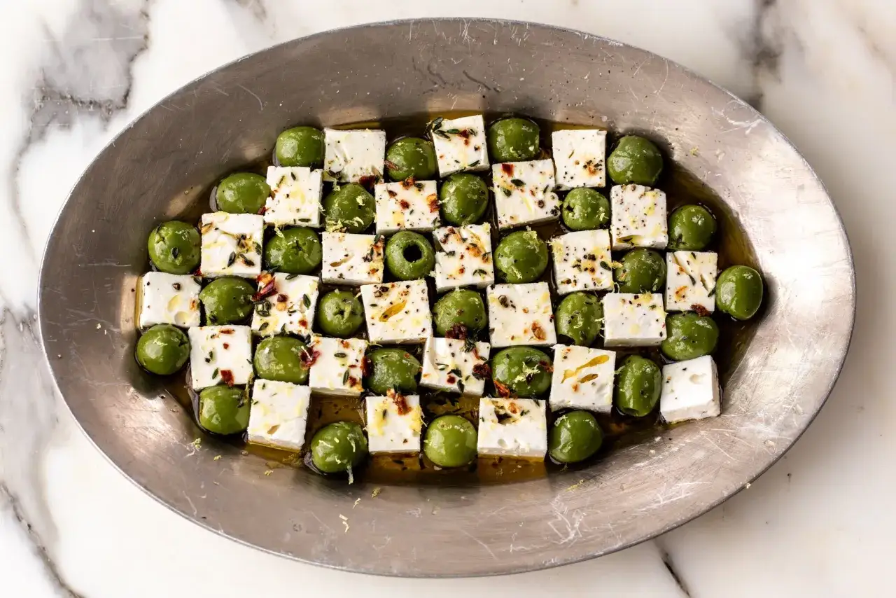 Grüne Oliven und gewürfelter Feta in Öl mariniert, mit Kräutern und Gewürzen bestreut. Ein köstlicher Appetizer zum Oliven essen.