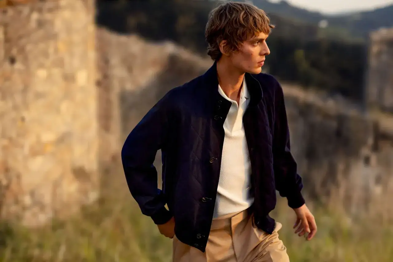 Junger Mann im preppy Look: Dunkle Steppjacke, weißes Polo und beige Hose.