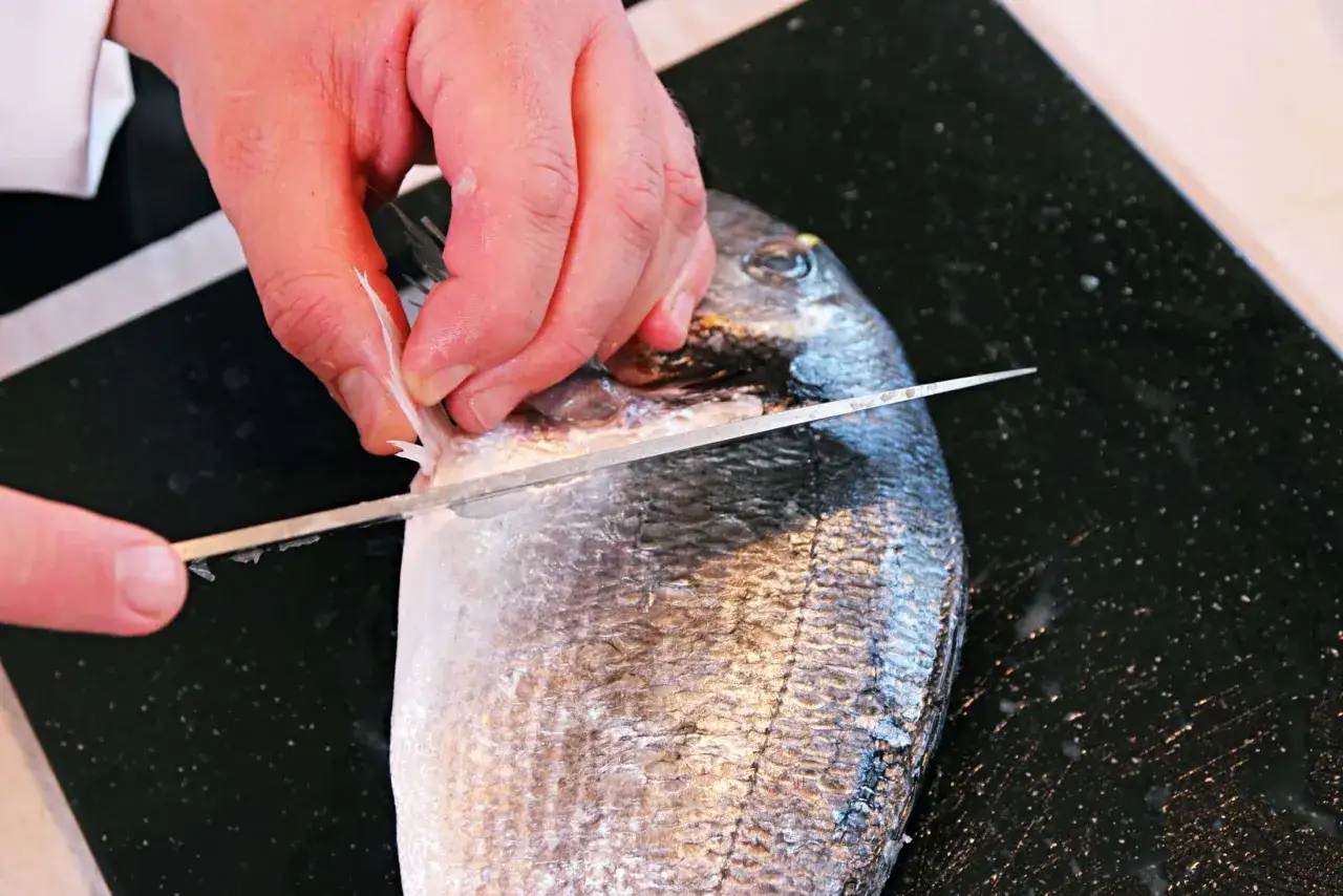 Hände filetieren einen frischen Fisch am Tisch mit einem scharfen Messer.