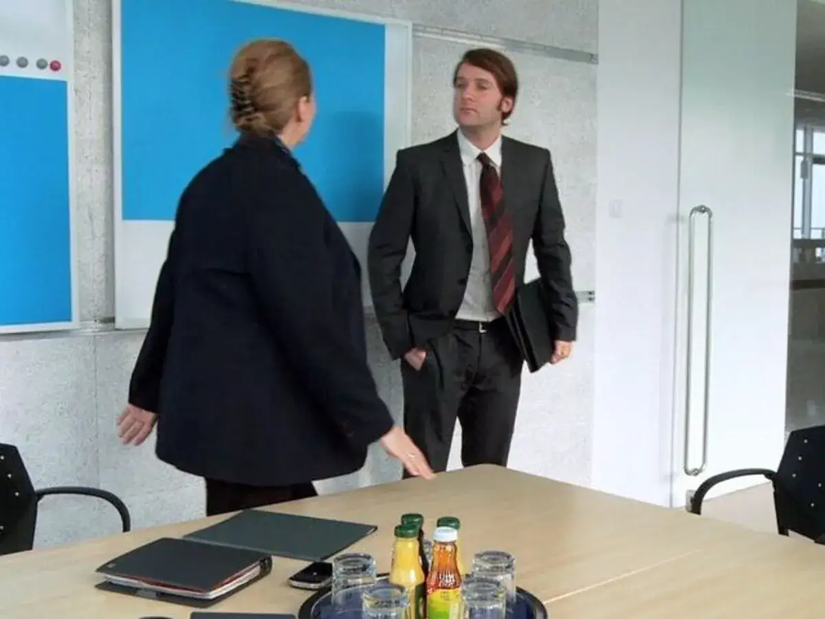 Mann im Anzug und Frau im dunklen Blazer verabschieden sich in einem Büro.