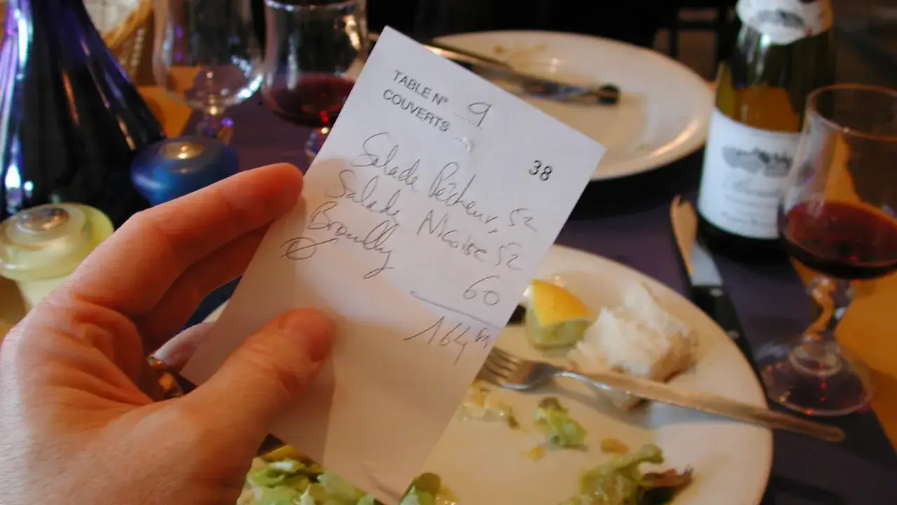 Hand h&auml;lt Rechnung mit Speisen und Preisen. Nach dem Essen in Holland &uuml;berlegt man, wie viel Trinkgeld angemessen ist.