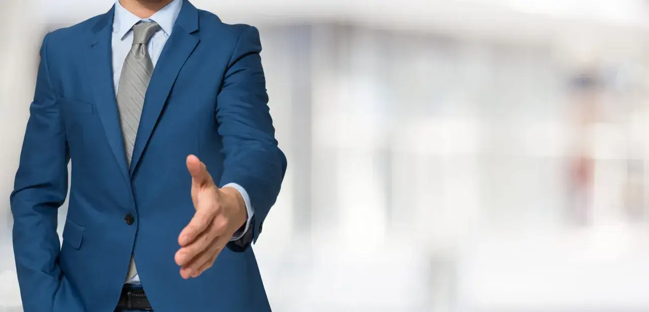 Mann im blauen Anzug streckt die Hand zum Hand geben aus.